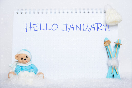 HELLO JANUARY. Teddy bear on a sled, blue wooden skis, a white hat and a notebook with the words HELLO JANUARY