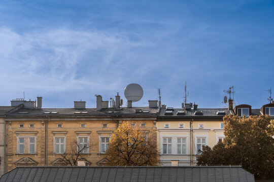 In the autumn sky, a hot air balloon rises over the roofs of houses on the street of Krakow, the sunlight illuminates the branches of autumn trees, the background image of the urban landscape