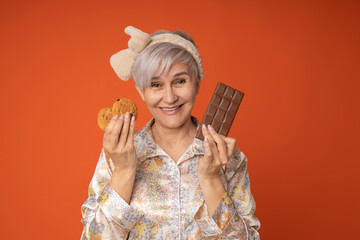 portrait of an elderly woman in pajamas with cookies and chocolate