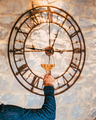 Une main de femme qui tient un verre de vin rosé dans la main sur arrière plan d'horloge ancienne accrochée au mur