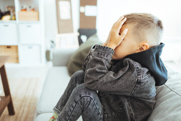 Young preteen teenager boy holding his had in his bedroom with smartphone, Cyber bullying in kid,...