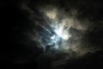 Naklejka na ściany i meble Partial solar eclipse behind clouds. The moon partially covers the sun. Natural, rare phenomenon seen 25 October 2022. 