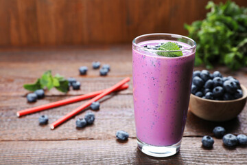 Glass of blueberry smoothie with mint on wooden table, space for text