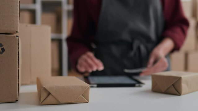 Packing warehouse worker glues a barcode on a boxed product, E-commerce sale online, Electronic tablet accounting of orders in a warehouse storekeeper works
