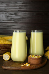 Tasty fresh corn milk in glasses and cobs on wooden table
