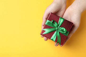 Woman holding beautifully wrapped Christmas gift box on yellow background, top view. Space for text