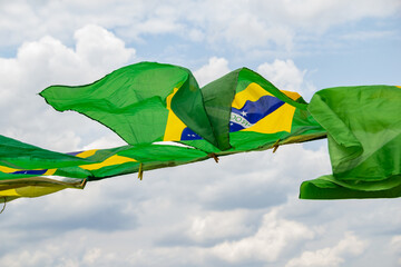 Algumas bandeiras do Brasil balançando ao vento com o céu nublado ao fundo.