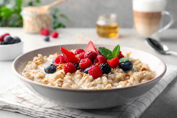 Bowl of oatmeal porridge served with berries on light grey table, closeup