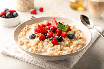 Bowl of oatmeal porridge served with berries on light grey table, closeup