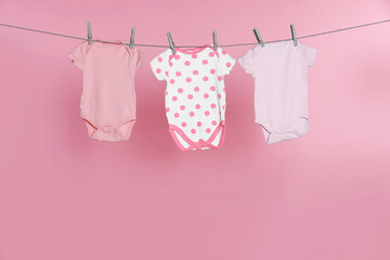 Baby onesies drying on laundry line against pink background