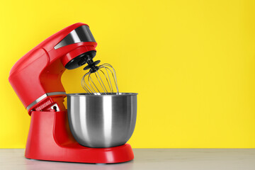 Modern red stand mixer on white wooden table against yellow background, space for text