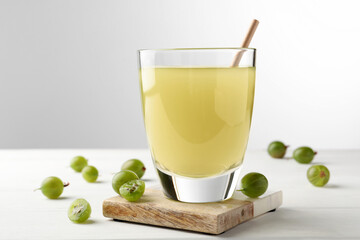 Tasty gooseberry juice on white wooden table against light background