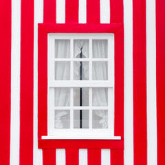 Old wooden window with white frame on the background of the striped red and white wall. Portugal Windows. The exterior of Portuguese houses.