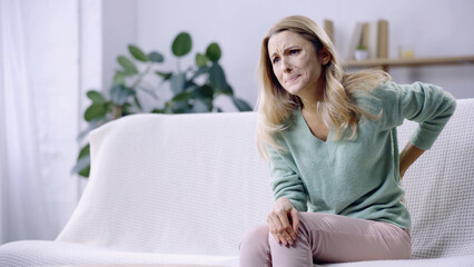 Obraz premium sad woman having pain in back while sitting on couch in modern living room