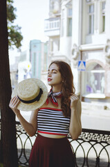 Fashion portrait of young, happy, elegant redhead curly woman, girl in hat and casual clothes. French style. Walking, relax in the city street. Sunny day.