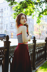 Fashion portrait of young, happy, elegant redhead curly woman, girl in hat and casual clothes. French style. Walking, relax in the city street. Sunny day.