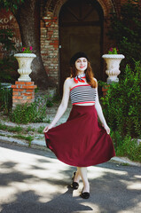 Fashion portrait of young, happy, elegant redhead curly woman, girl in hat and casual clothes. French style. Walking, relax in the city street. Sunny day.