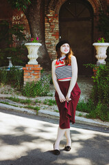 Fashion portrait of young, happy, elegant redhead curly woman, girl in hat and casual clothes. French style. Walking, relax in the city street. Sunny day.