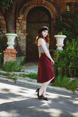 Fashion portrait of young, happy, elegant redhead curly woman, girl in hat and casual clothes. French style. Walking, relax in the city street. Sunny day.
