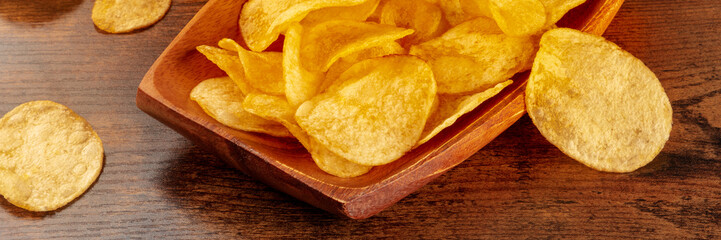 Potato chips or crisps, a salty snack on a wooden table, a panoramic banner