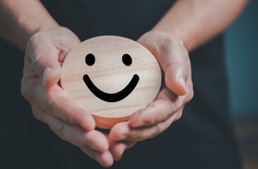 Hands holding wooden happy smile face, good feedback rating and positive customer review,experience, satisfaction survey,mental health assessment,child feeling good,world mental health day. - 540962326
