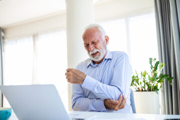 Shot of a businessman holding his elbow in pain while seated at his desk, hand pain
