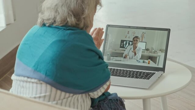 Over The Shoulder Shot Of Elderly Woman Having Online Consultation With Female Doctor Via Video Call On Laptop