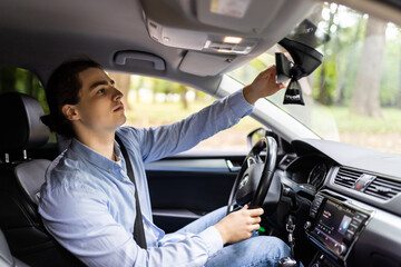 Confident young man executive adjusting rear view mirror driving alone in luxury car, back view, reflection