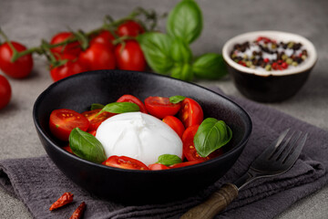 Burrata cheese with tomatoes and basil on a gray kitchen table.