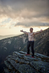 Bare-chested middle-aged man on top of rocky mountains