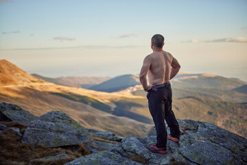 Bare-chested middle-aged man on top of rocky mountains