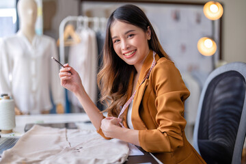 Young professional clothes fashion designer sitting near sewing machine use laptop computer and tablet pc to reference design smiling portrait to camera