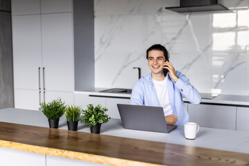Gig economy concept. Young positive man freelancer working remotely at home, looking at laptop and...