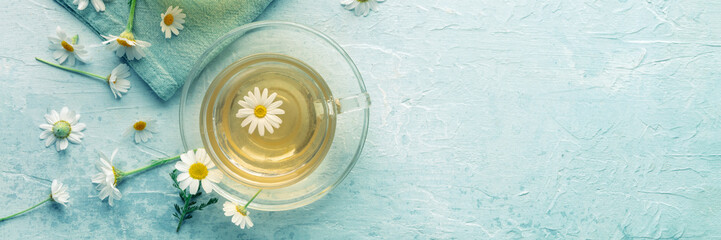 Chamomile tea in a cup with loose flowers, herbal medicine treatment, overhead flat lay panorama...