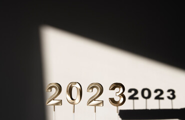 Festive background with gold numbers 2023 against a gray wall and an abstract window shadow. Beautiful background for Christmas and New Year.