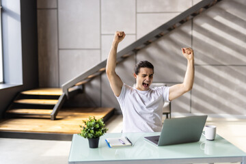 Fototapeta na wymiar Excited young man winner sit at home table looking at laptop screen celebrating online success victory euphoric overjoyed by internet sport bet win got new job opportunity or loan approval in email