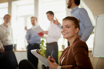 Focus on young and successful business lady. Happy smart girl in business suit in modern office during meeting with colleagues