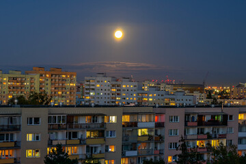 Pełnia księżyca nad miastem. Wieczór, światła w oknach bloków mieszkalnych.