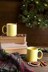 Obraz na płótnie Canvas books and two yellow cups near wreath with cinnamon near christmas decorations on wooden table