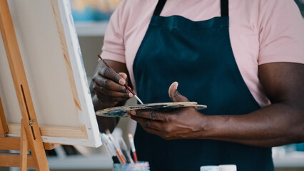 Close-up of male hands unrecognizable African man artist painter holding palette with bright oil acrylic paints colors drawing creates picture on canvas and easel using painting with brushes draw