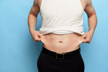 Naklejka premium Cropped image of man showing his belly, abdomen. Close Up part of man's body. Concept of dieting, sport, fitness, healthy lifestyle, body positive