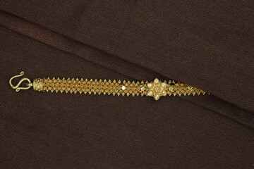 Gold bracelet with flowers on a reddish-brown fabric background.