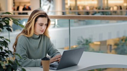 Caucasian business female freelancer student designer worker sitting at table in cafe office corporate space working with laptop typing message drinking coffee tea e-learning online shopping free wifi