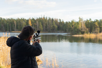 A man in a black jacket with a gun in his hands aims at the background of the lake.