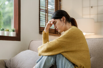 Asian woman with a headache and stress while sitting on the sofa at home