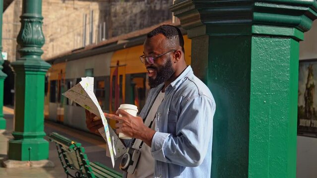 Young African American man with map and coffee at European terminal train station. Tourist travel by train on vacation time holiday weekend trip.