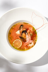 Traditional italian fish soup with shrimp, mussels and salmon. Seafood soup on white background. Tom yam kung with seafood. Spicy fish soup with prawns and lime on light background. Trendy food.