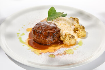 Fototapeta na wymiar Beef cutlet with grilled cauliflower with gravy and cheese sauce on white plate. Elegant beefsteak on light background with shadows of sunlight. Summer menu with hard shadows Meat ball of minced meat