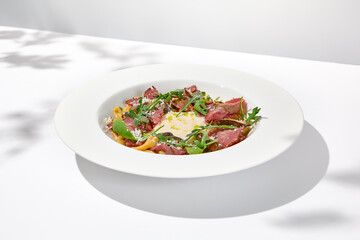 Homemade pasta with pastrami and creamy sauce with cheese. Italian pasta pappardelle with beef and sauce on white table Italian food in summer dining with shadows of sunlight