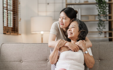 Fototapeta premium Elderly mother and grown daughter holding hands sitting on the sofa hugging.